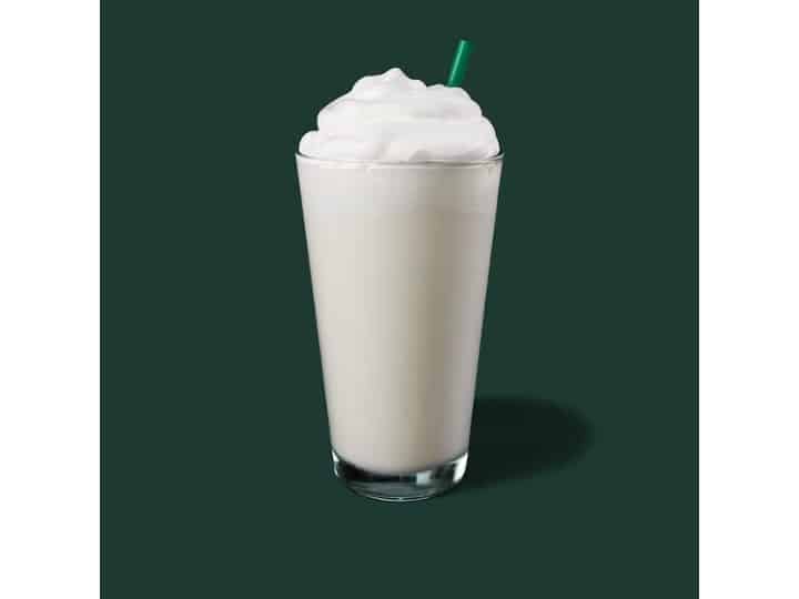 A clear glass of starbucks vanilla creme frappuccino with whipped cream on top.