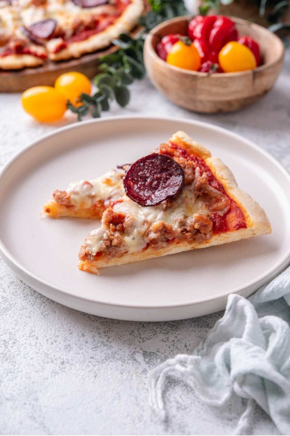 A slice of protein pizza topped with cheese, pepperoni, and sausage on a white plate. There is a bite taken out of the slice.