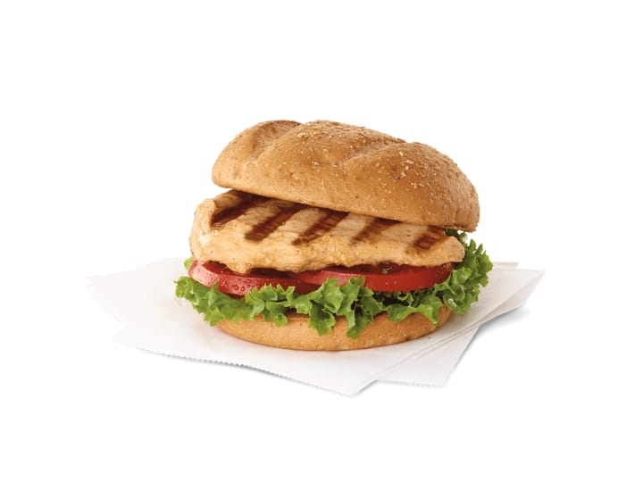 A grilled chicken sandwich with lettuce and tomato on a napkin.