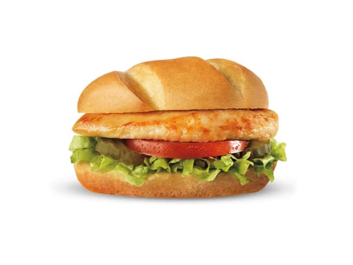 A bun with lettuce, tomato, pickles and a piece of grilled chicken.