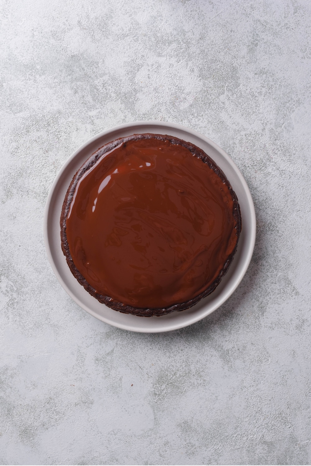 An overhead shot of a whole chocolate protein cake coated with melted chocolate ganache.