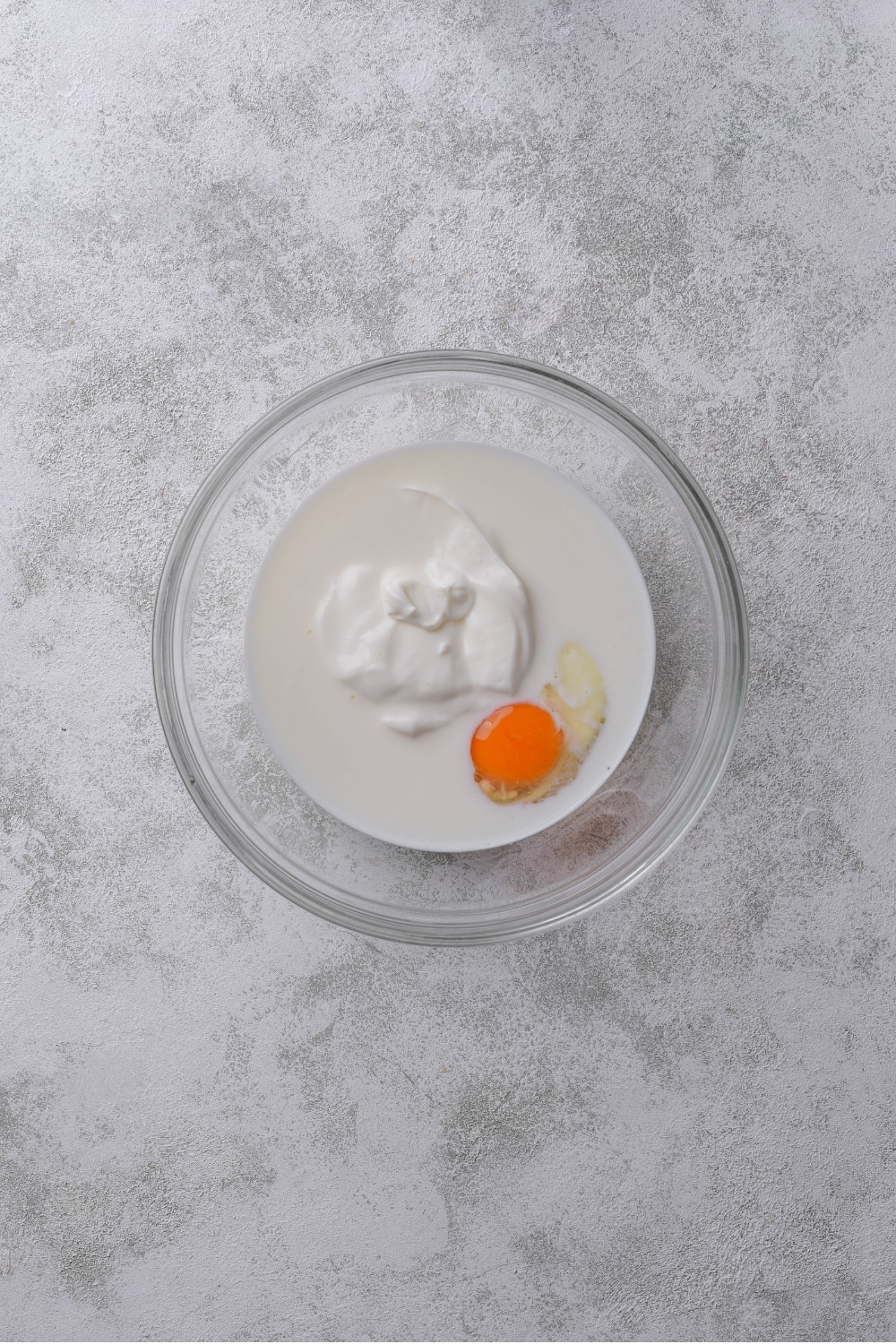 An overhead shot of a glass bowl filled with raw egg, greek yogurt, and almond milk.