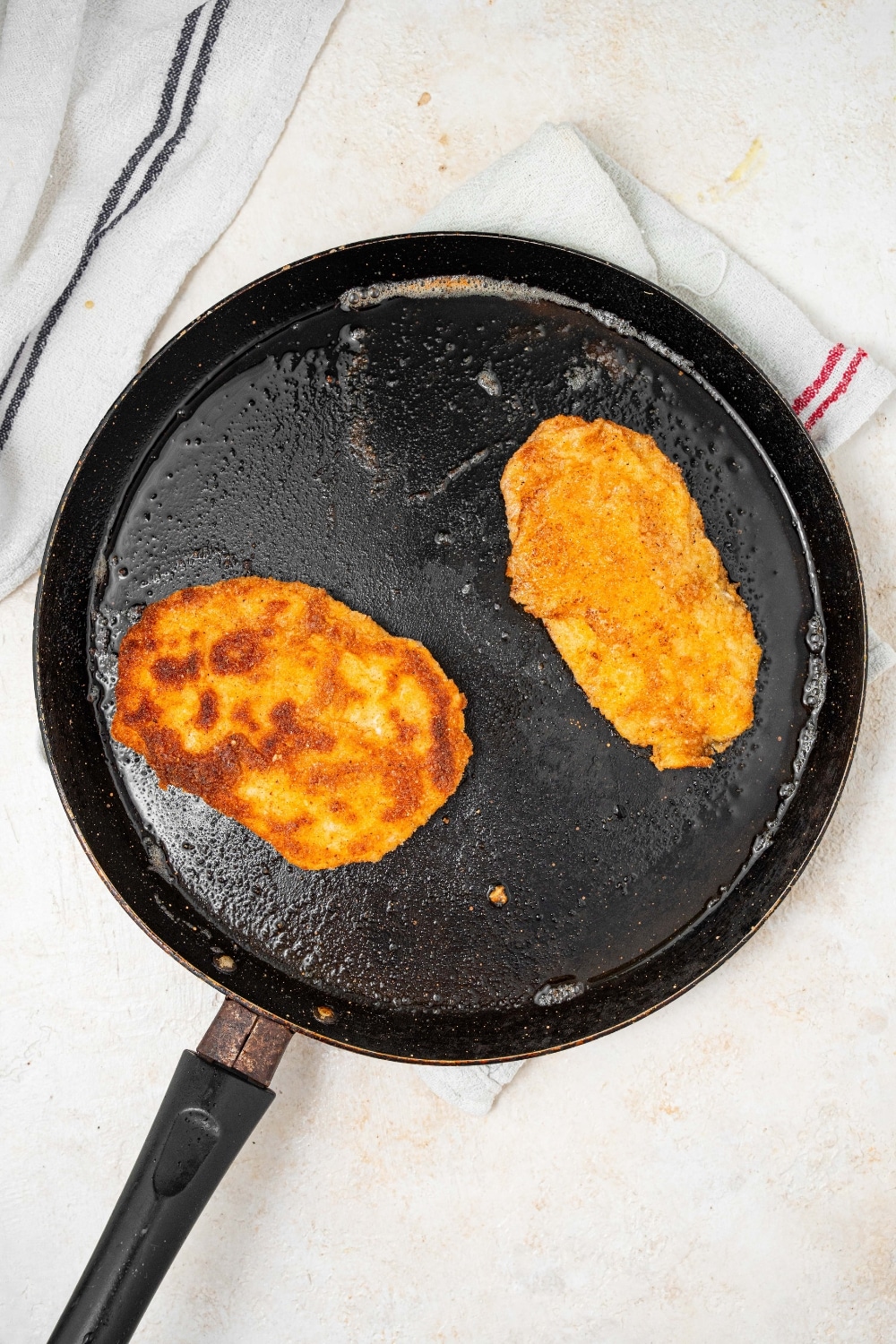 An overhead shot of a large skillet frying two breaded calamari steaks.