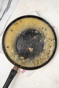 An overhead shot of a large skillet cooking a lemon caper sauce.