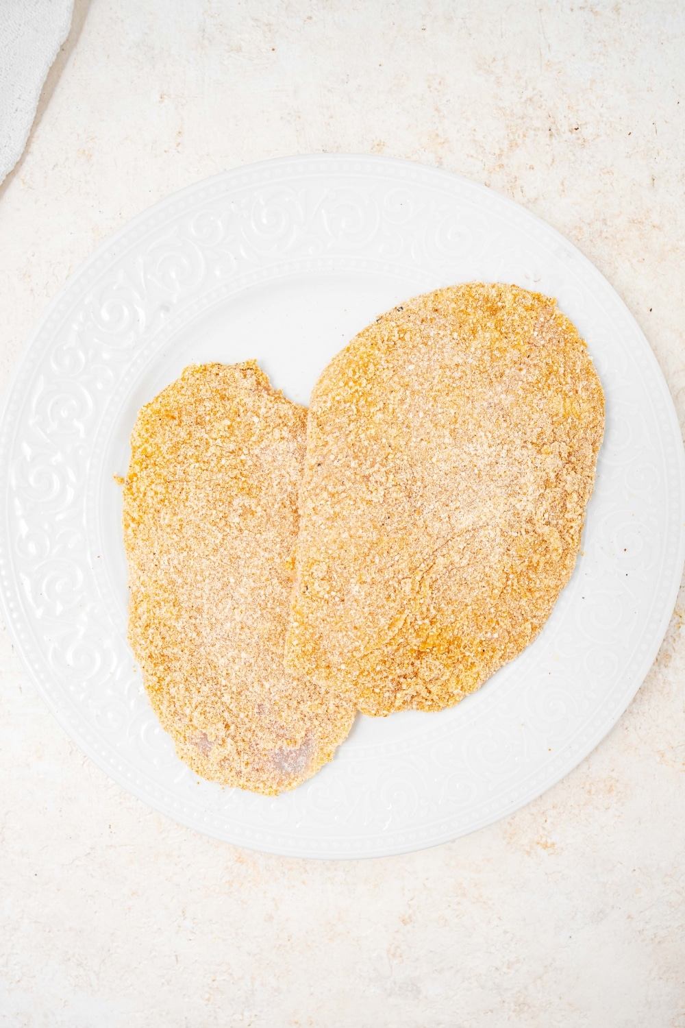 An overhead shot of a plate with two raw breaded calamari steaks.