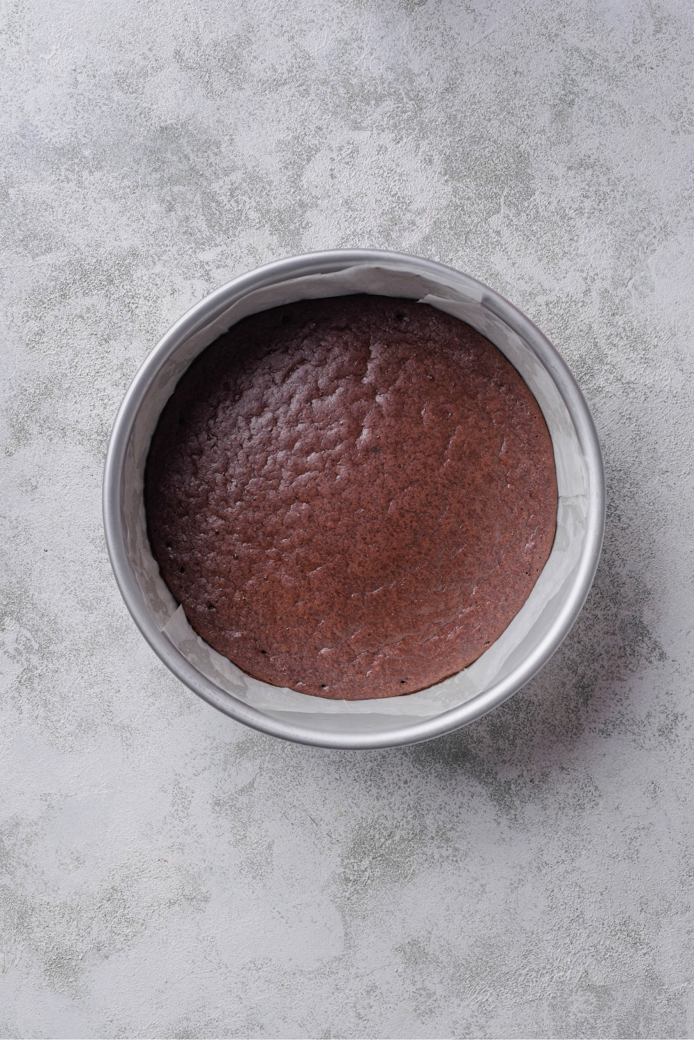 An overhead shot of a cake pan lined with parchment paper filled with a cooked chocolate protein cake.