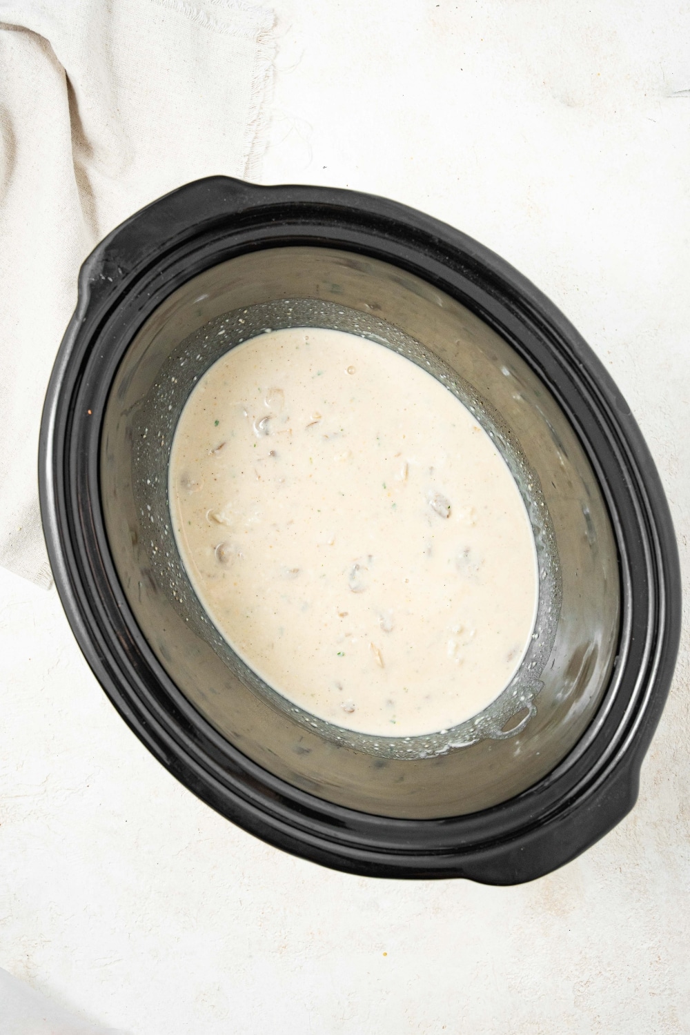 An overhead shot of a slow cooker filled with beef broth and cream of mushroom soup mixture.