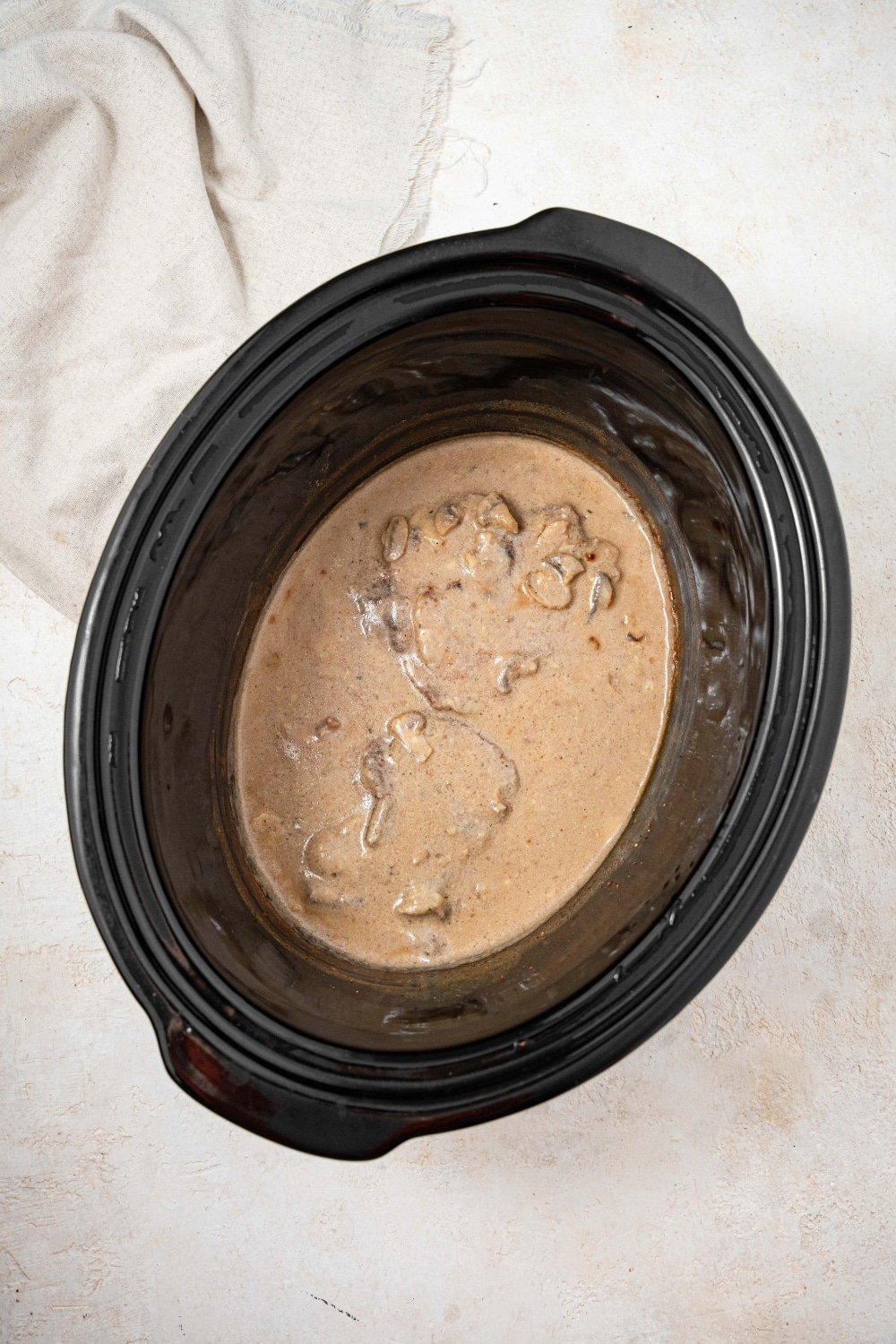 An overhead shot of a slow cooker filled with cube steaks cooking in a thickened gravy.