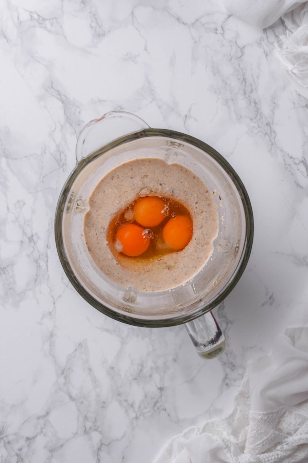 An overhead shot of a glass blender filled with a high fiber pancake batter and three raw eggs.