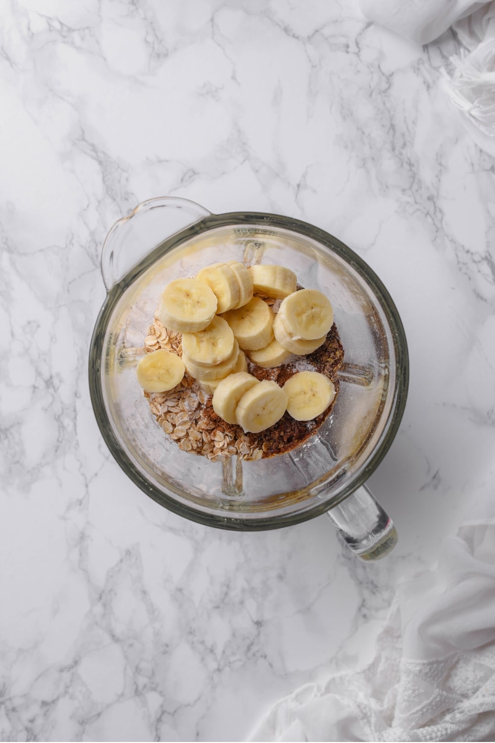 An overhead shot of a glass blender filled with oats and sliced banana.