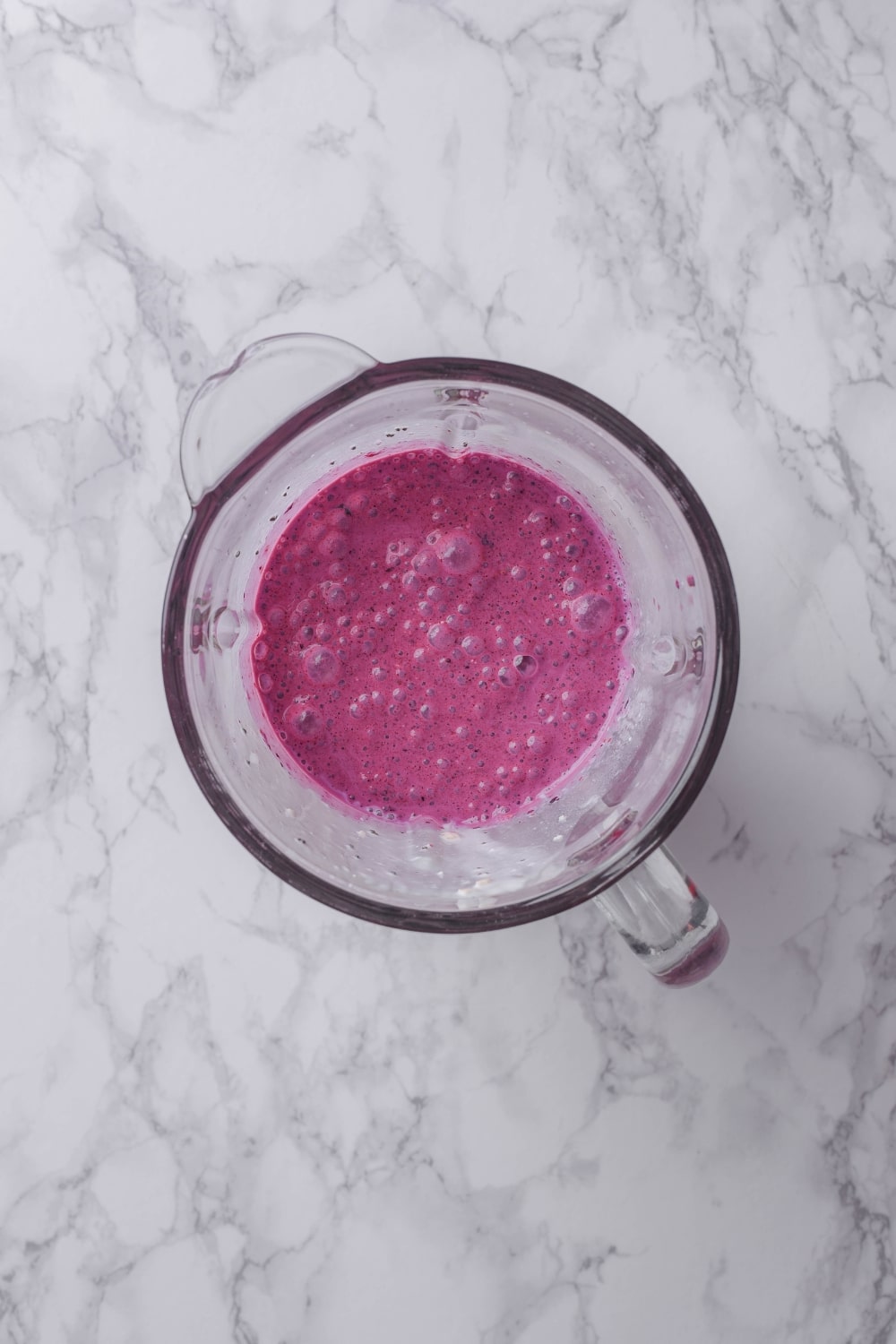 An overhead shot of a glass blender filled with a blended blueberry smoothie mixture.