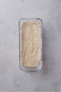 An overhead shot of a glass loaf pan filled with raw protein bread dough.