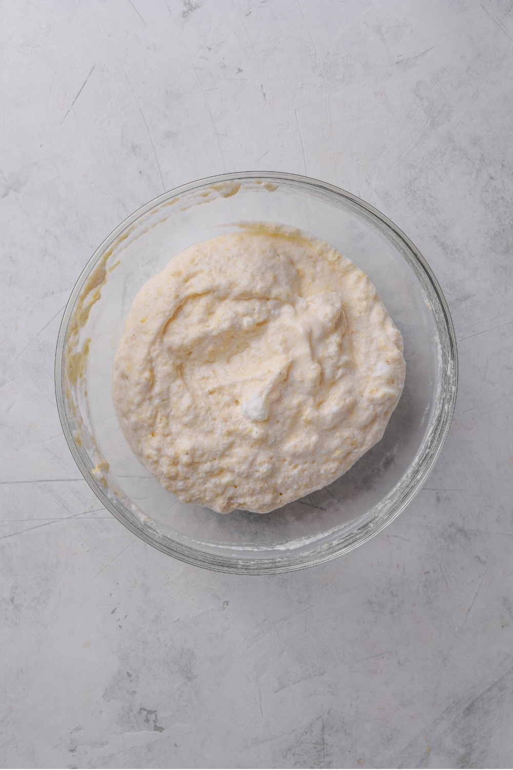 An overhead shot of a large glass bowl filled with a raw protein bread dough mixture.