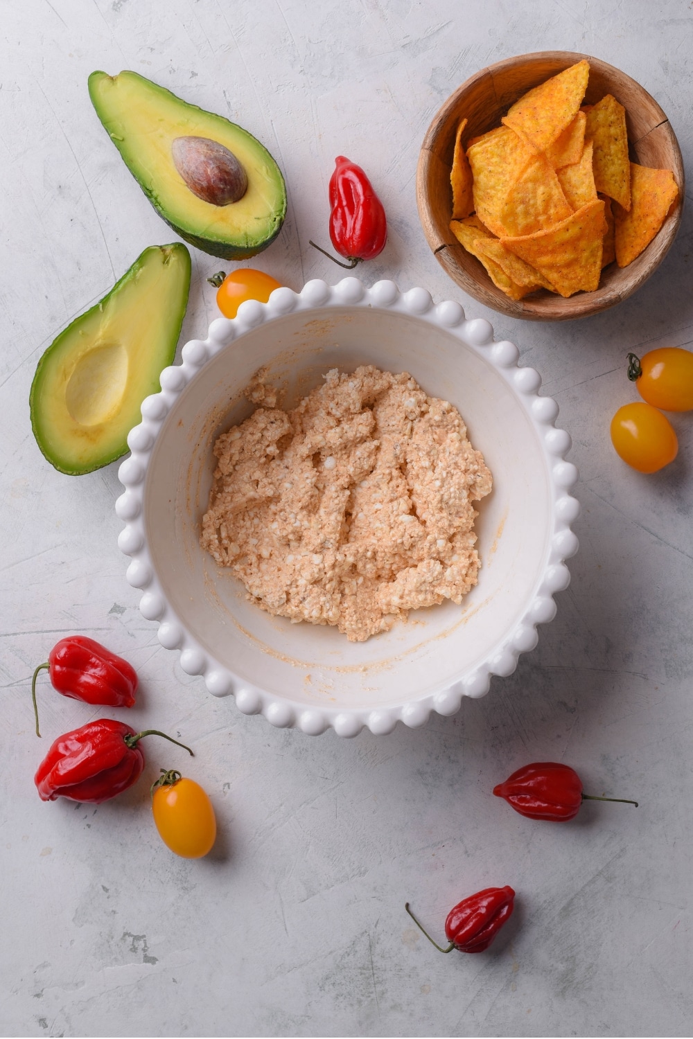 An overhead shot of a bowl of queso dip mixed together. There is a smaller bowl of tortilla chips next to the dip along with a halved avocado on the side.