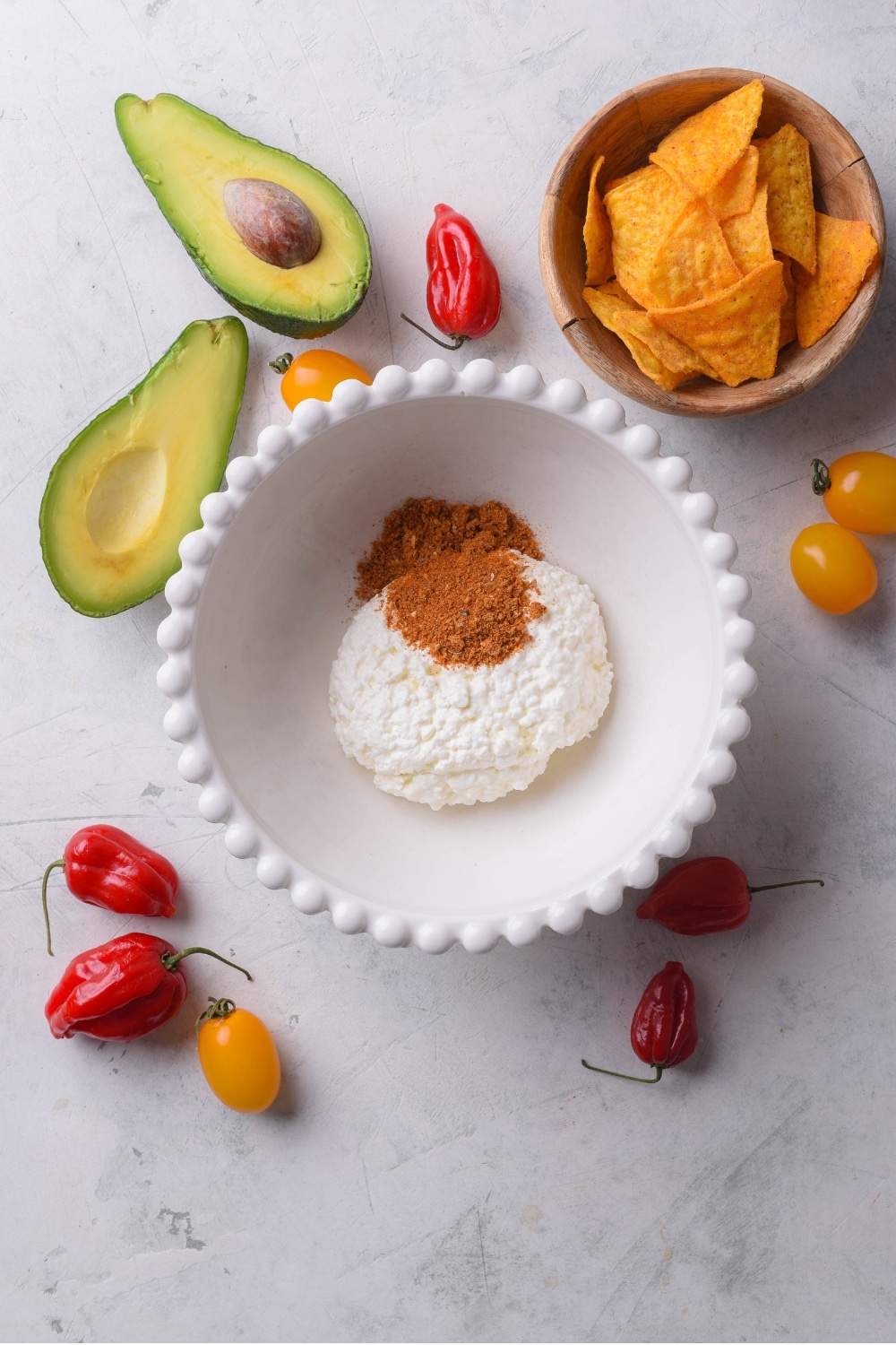 An overhead shot of a bowl of a cottage cheese with taco seasoning on top. There is a smaller bowl of tortilla chips and a halved avocado next to the bowl.