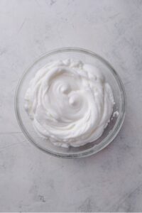 An overhead shot of a large glass bowl filled with beaten egg whites.