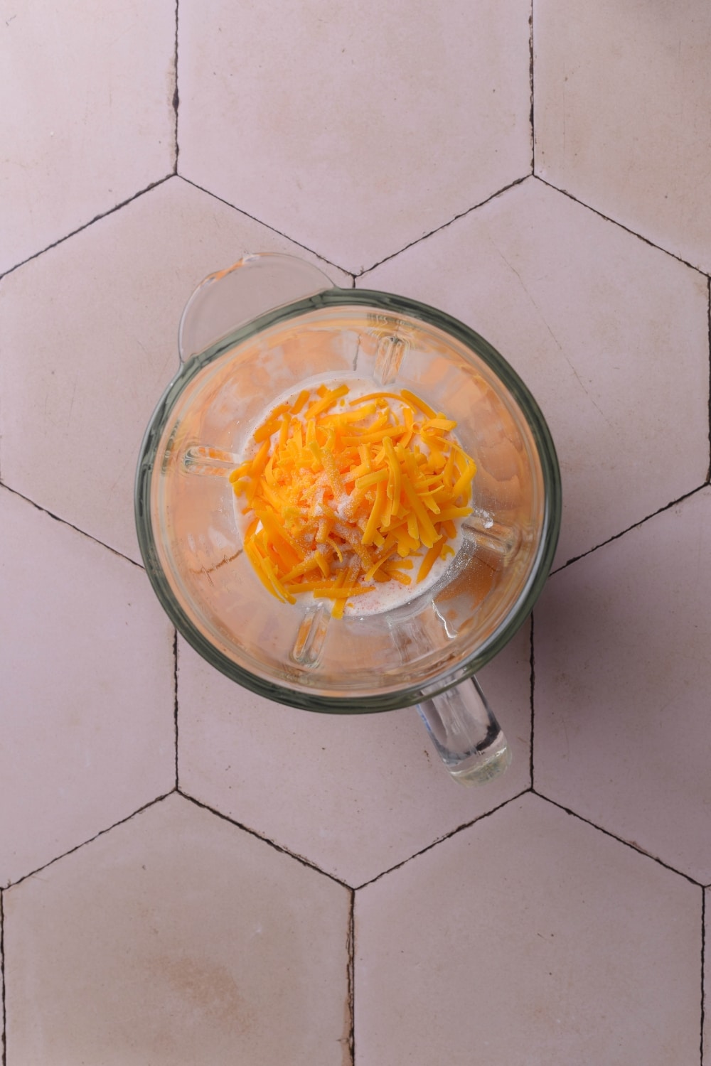 An overhead shot of a blender filled with milk, shredded cheddar cheese, and cottage cheese.