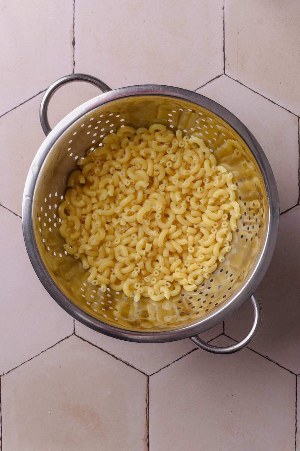 An overhead shot of a metal colander filled with drained elbow macaroni.