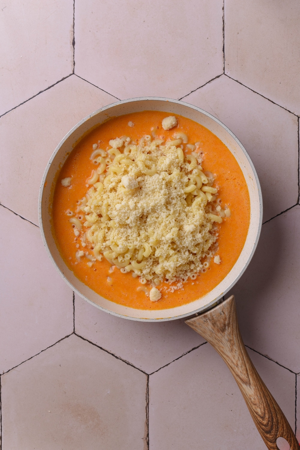 An overhead shot of a ceramic pan filled with cheese sauce. Elbow macaroni and grated cheese sit on top of the sauce.