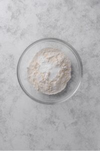 An overhead shot of a glass bowl filled with flour, baking powder, and salt.