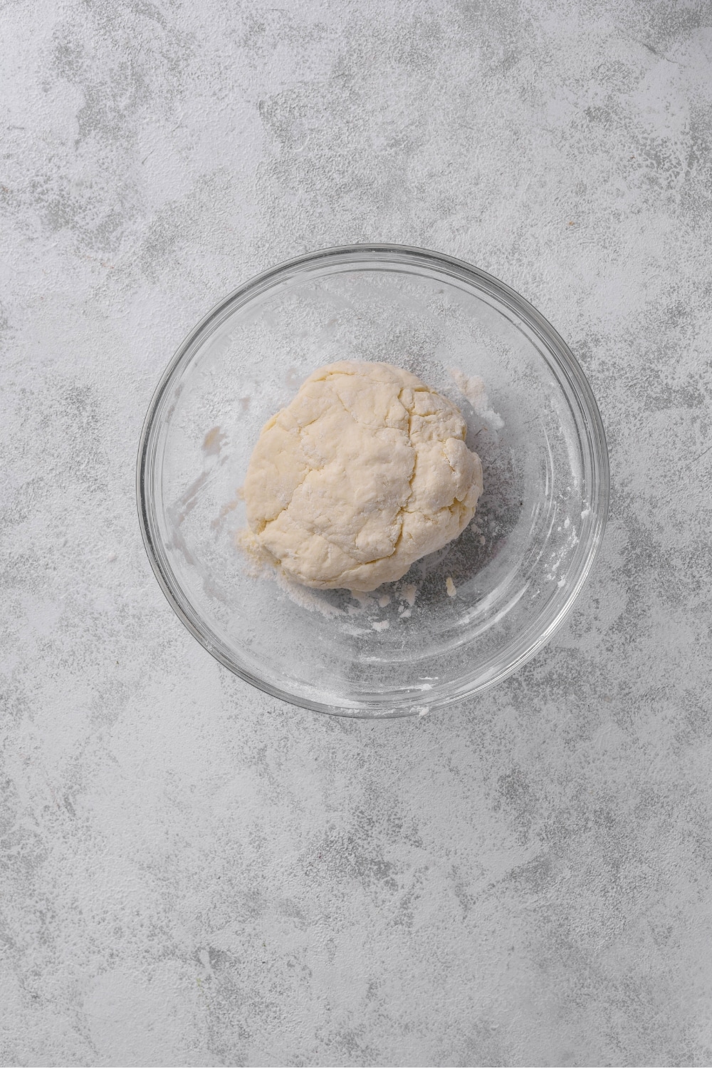 An overhead shot of a glass bowl with a ball of protein pizza dough.