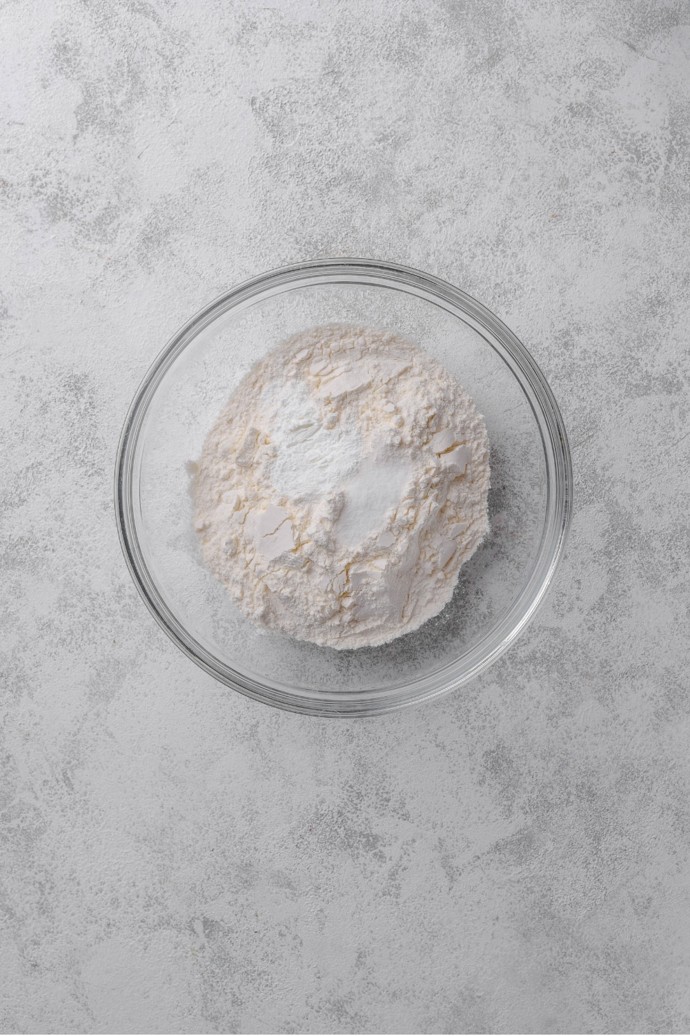 An overhead shot of a glass bowl filled with flour, baking powder, and salt.