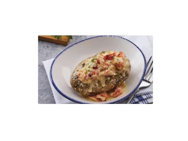 Lobster topped on a baked potato in a bowl.