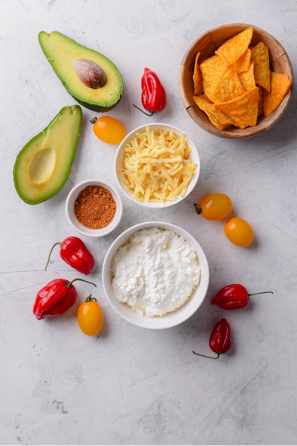 An overhead shot of several bowls holding various ingredients for low calorie queso dip including cottage cheese, shredded monterey jack, and taco seasoning.