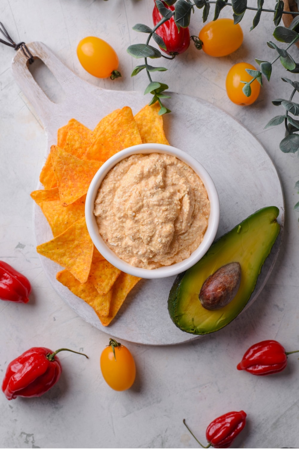 An overhead shot of a bowl of low calorie queso dip served on a wooden server with tortilla chips and a halved avocado.