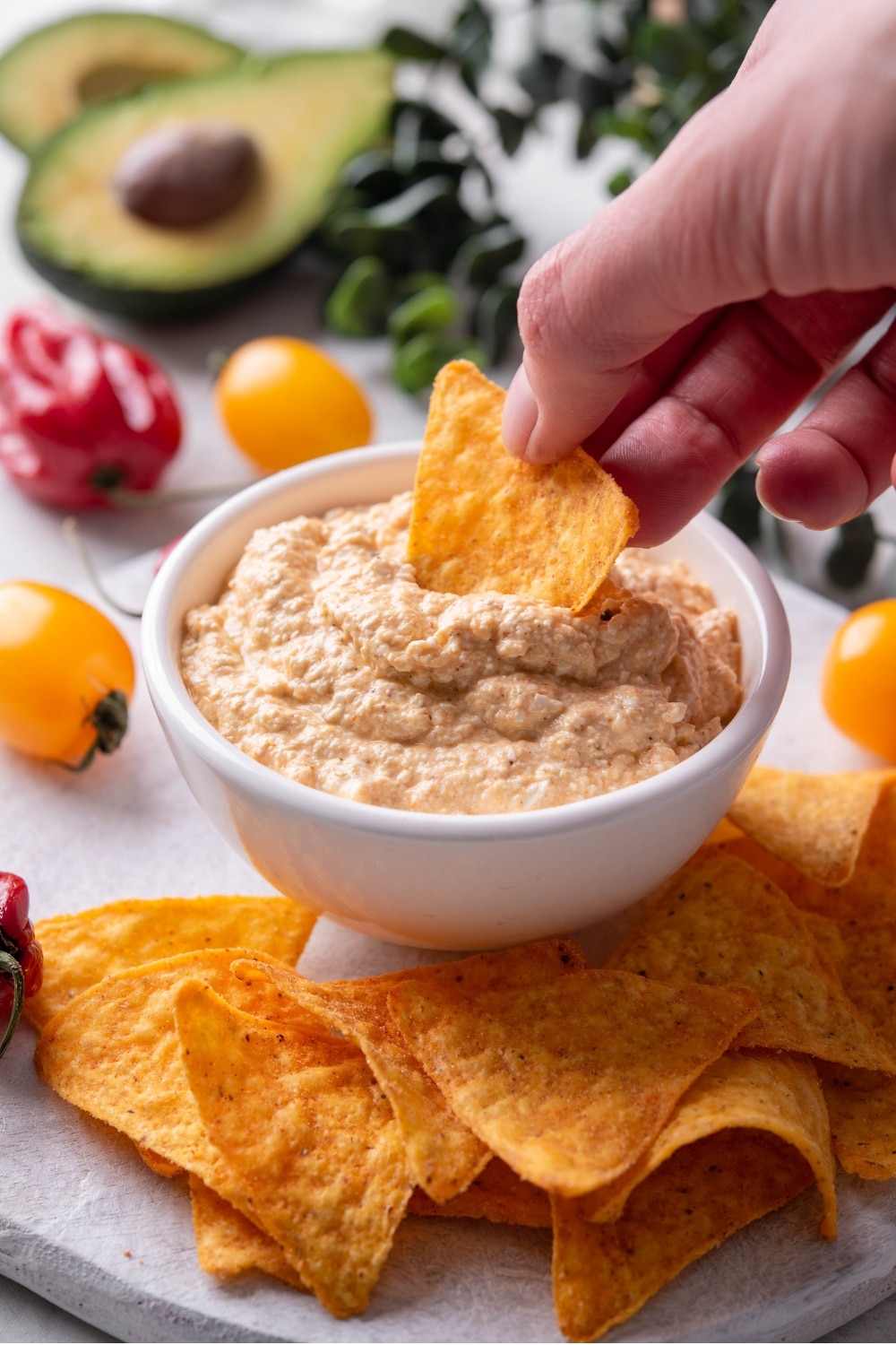 A bowl of low calorie queso dip on a wooden serving board with tortilla chips. There is a hand inserting a tortilla chip into the queso.