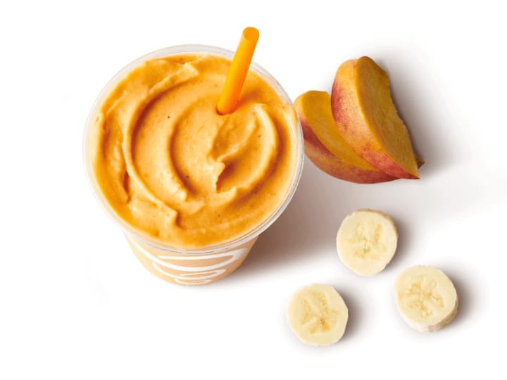 An orange smoothie in a cup with bananas and orange slices next to it.