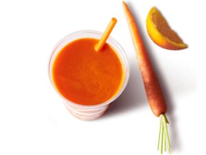 A cup of carrot juice with a carrot and orange next to it.