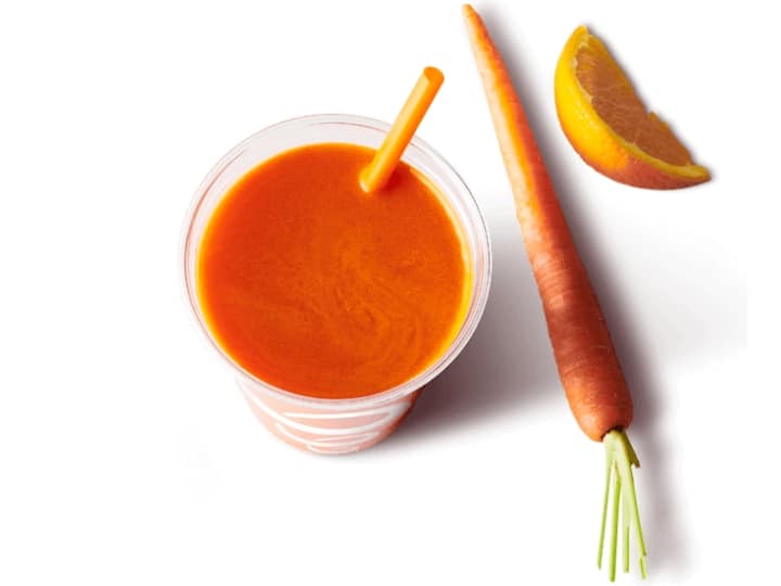 A cup of carrot juice with a carrot and orange next to it.