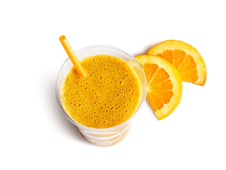 An orange juice drink in a cup with orange slices next to it
