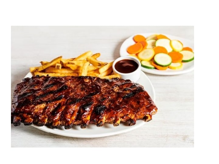 A bunch of baby back ribs on a white plate.