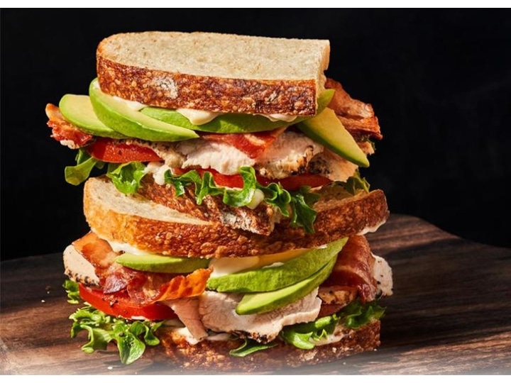 A sandwich with avocado, turkey, bacon, lettuce, and tomato stacked on top of each other.