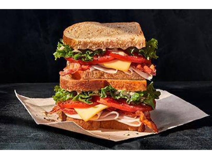 A turkey, cheese, lettuce, and tomato sandwich cut in half, stacked on top of one another.