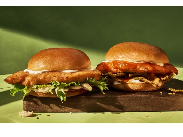 Two grilled chicken sandwiches on a wooden cutting board.