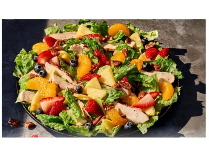 Chicken, mandarin oranges, apples, and strawberries on top of a salad.