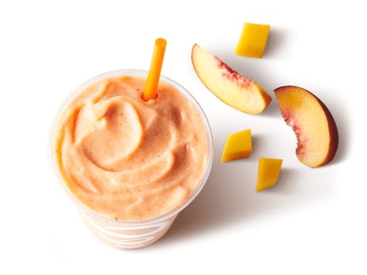 A peach smoothie in a cup with peaches next to it.