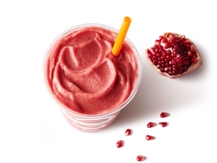 A pomegranate smoothie in a cup with a pomegranate next to it.