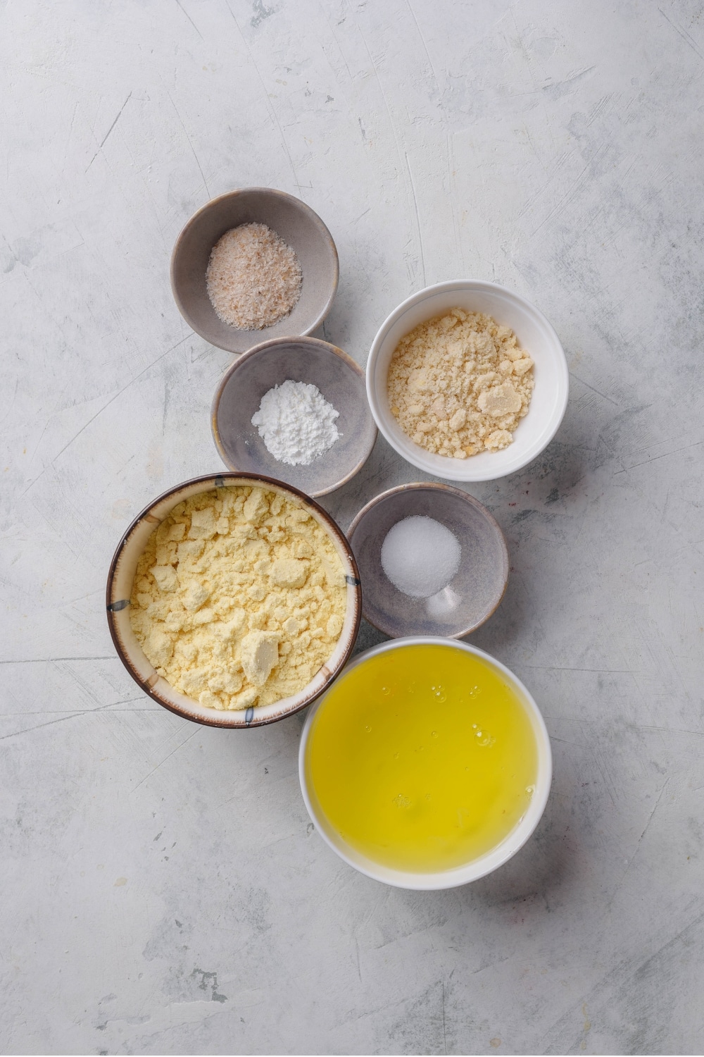 An overhead shot of several bowls of different shapes and sizes carrying various ingredients for protein bread including whey protein, egg whites, salt, baking powder, and almond flour.