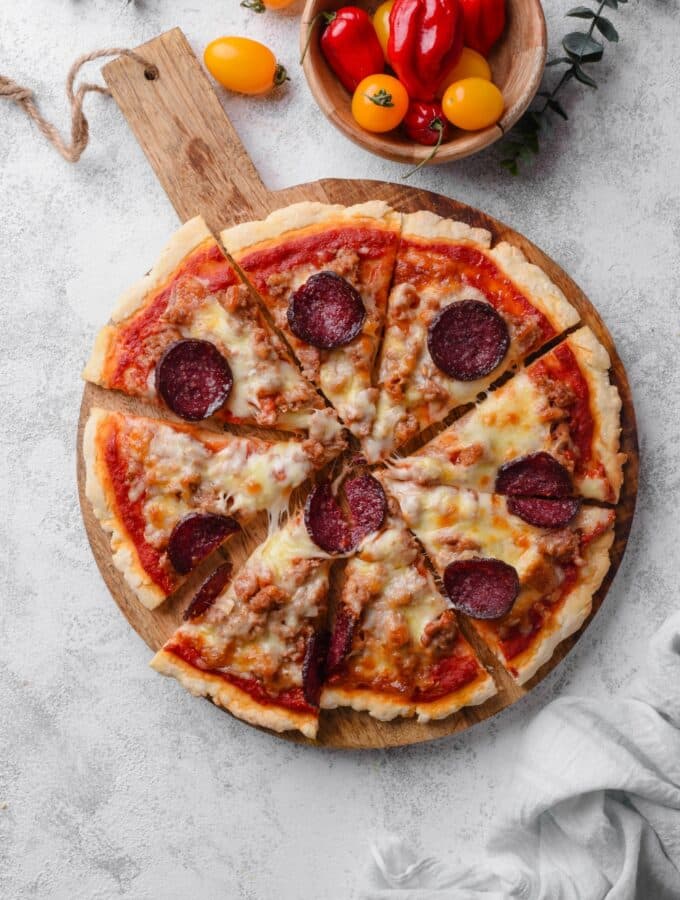 An overhead shot of a whole pizza sliced on a wooden server. The pizza is topped with cheese, pepperoni, and sausage.