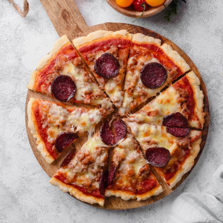 An overhead shot of a whole pizza sliced on a wooden server. The pizza is topped with cheese, pepperoni, and sausage.