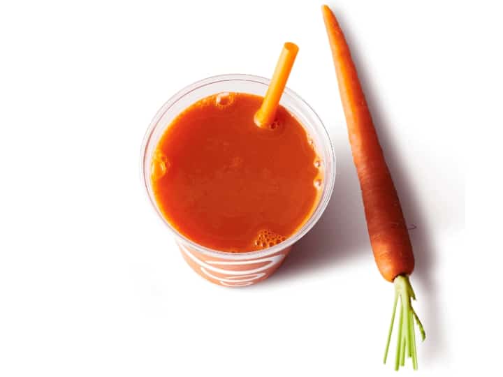 A cup of carrot juice with a carrot next to it.