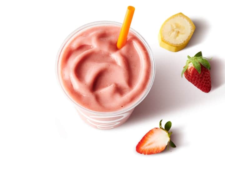 A strawberry smoothie in a cup with a strawberry and banana slice next to it.
