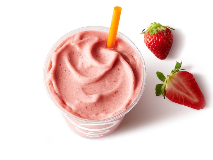 A strawberry smoothie in a cup with strawberries next to it.