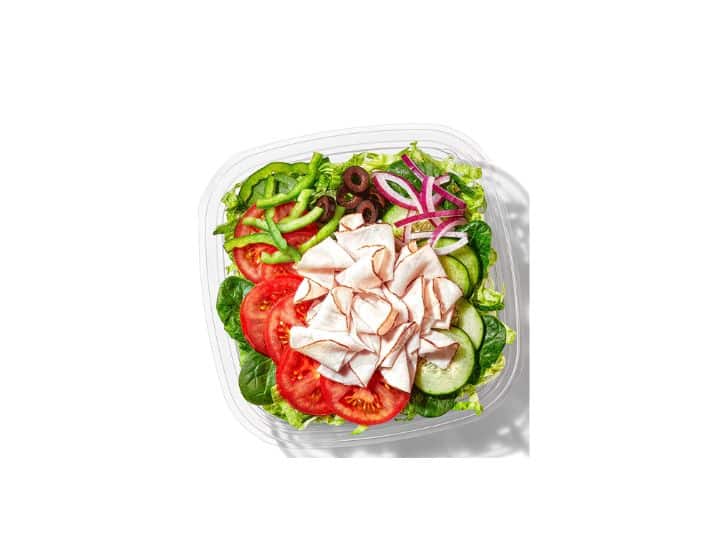 Sliced turkey, lettuce, tomato, cucumber, and red onion in a clear plate.