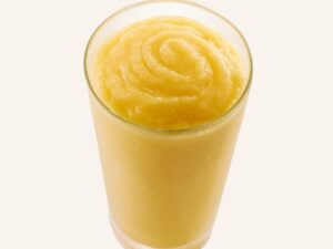 A yellow smoothie that is in a glass cup.