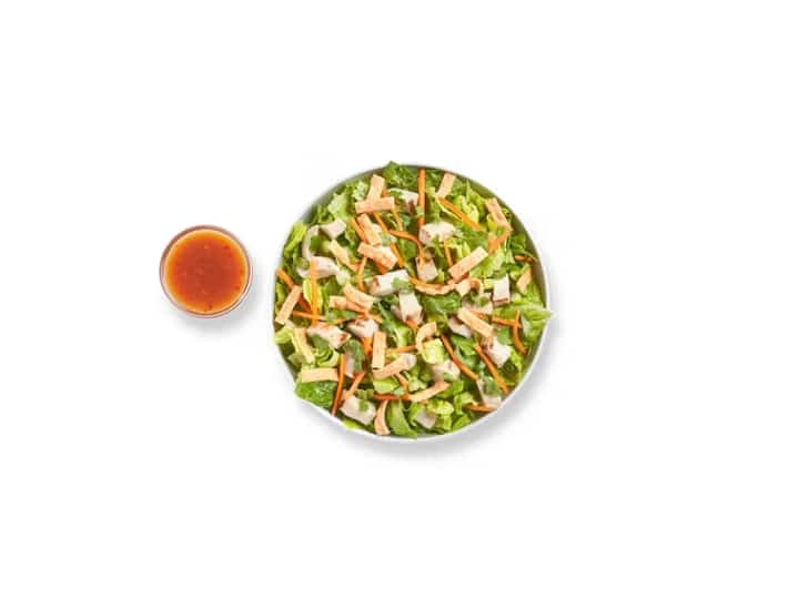 Grilled chicken on top of a Thai chicken salad with a cup of dressing next to it.